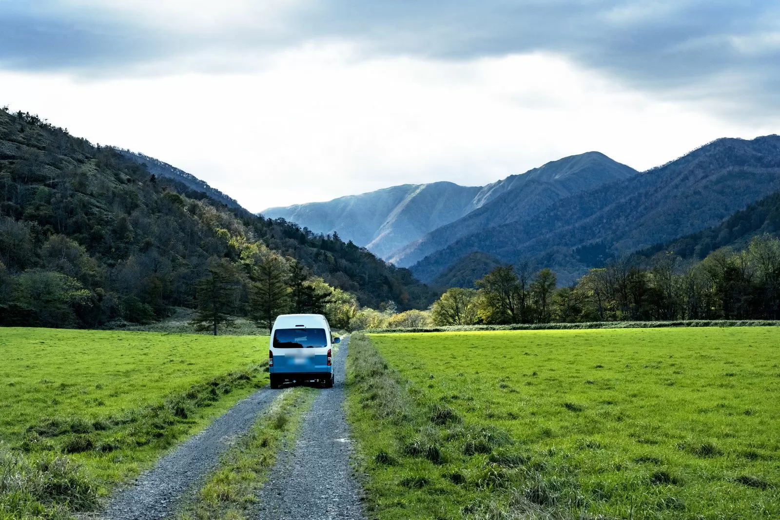 行駛在貫穿山間牧草地的未鋪裝道路上的露營車背影,兩側山巒綿延
