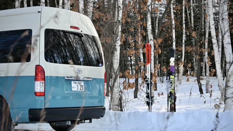 雪の白樺林に止めた白と青のハイエースのキャンピングカー