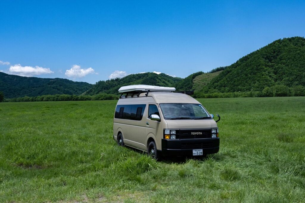 停在草原上、附車頂帳篷的米色露營車