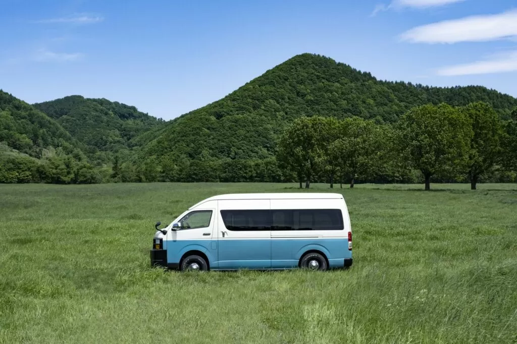 山と緑の草原に停まる白と水色のキャンピングカー