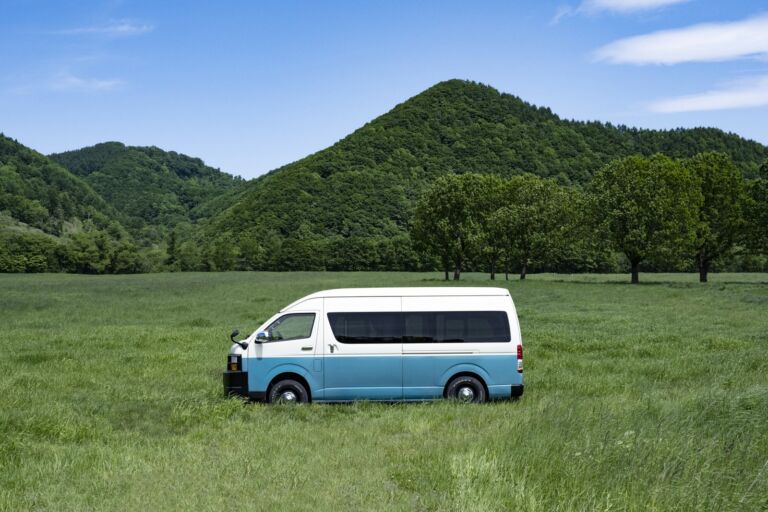 山と緑の草原に停まる白と水色のキャンピングカー