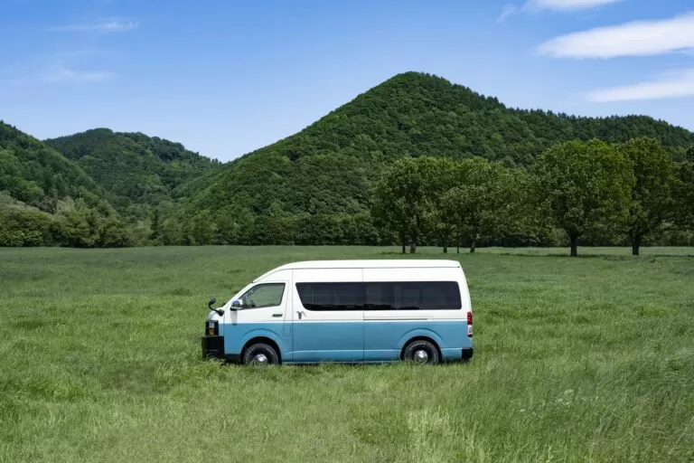 山と緑の草原に停まる白と水色のキャンピングカー