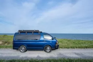 海沿いの砂利道に停まる青いキャンピングカー