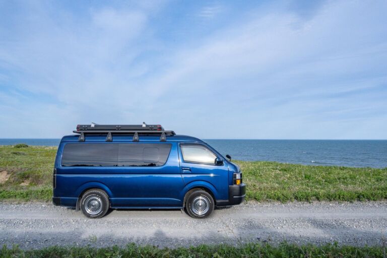 海沿いの砂利道に停まる青いキャンピングカー