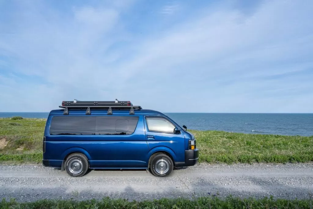 Blue campervan parked on a gravel road by the sea