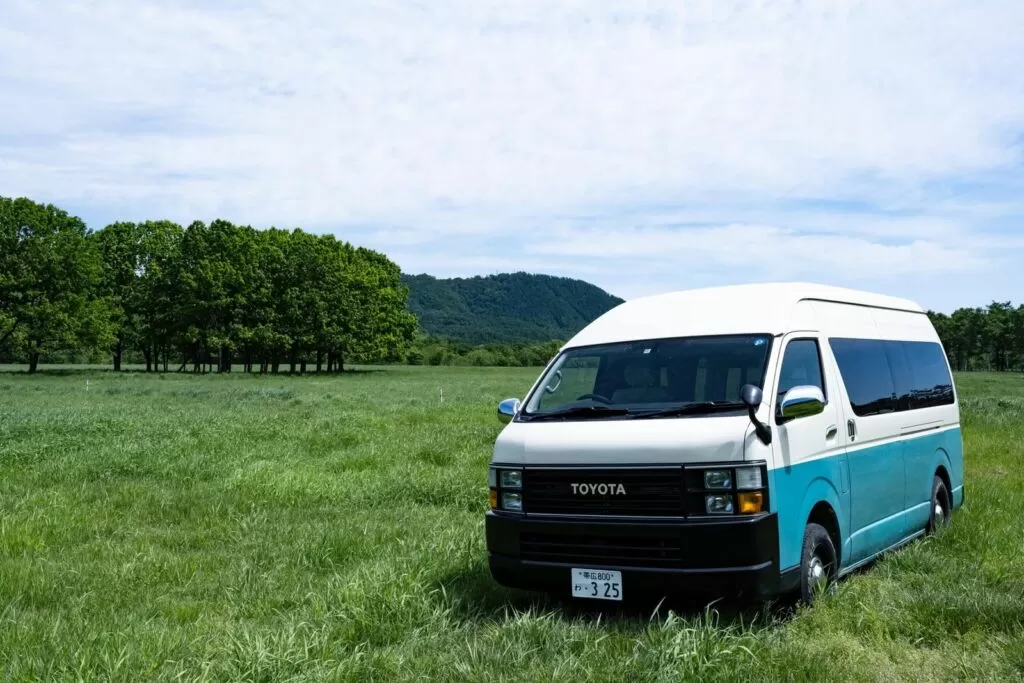 緑の草原に停まる白とターコイズのキャンピングカー