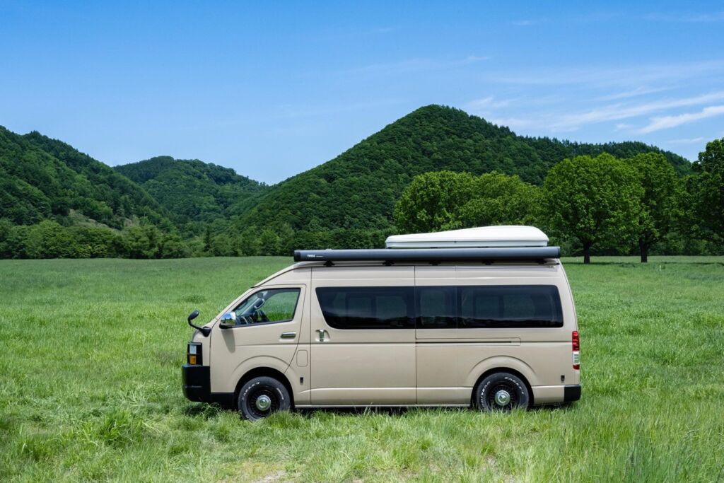 以山為背景、停在草原上的米色露營車（側面）