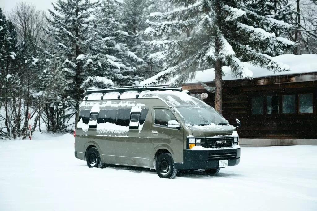 雪に覆われた丸太小屋の前に停まるキャンピングカー
