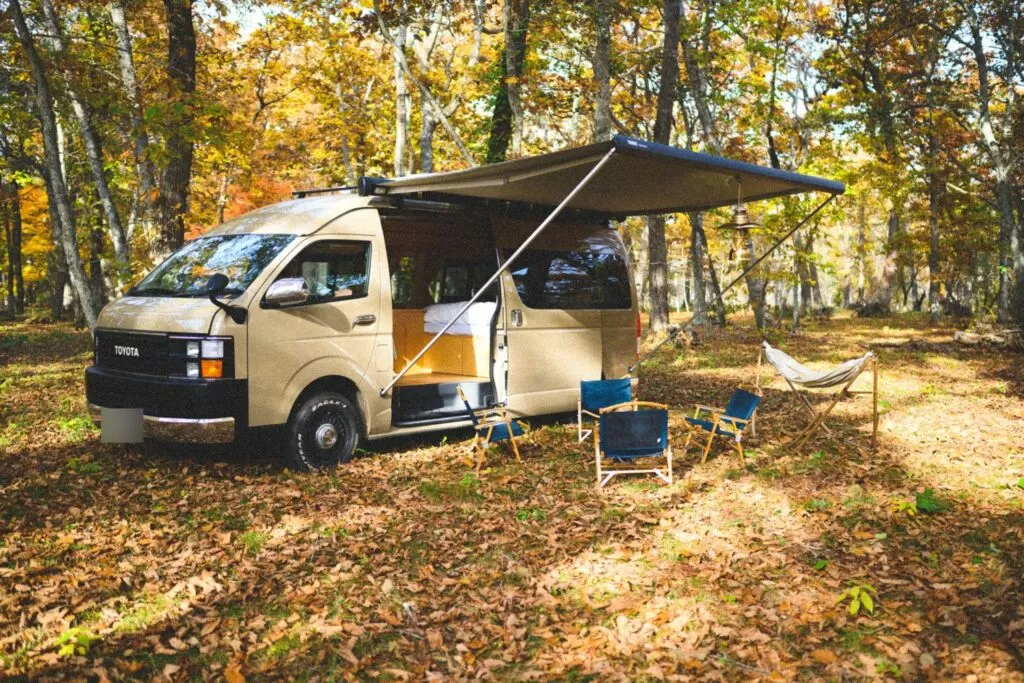 紅葉の森でタープを広げたキャンピングカー（Moving Inn の写真）