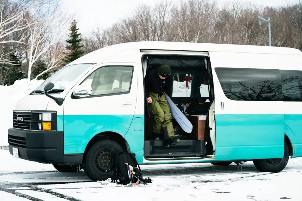 雪の駐車場で側面ドアを開けたハイエース系キャンピングカー