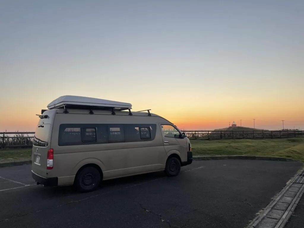 夕暮れの駐車場に停まるハイエース系キャンピングカー